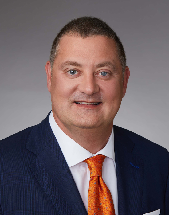 William Beynon, wearing a navy suit with a white shirt and bright orange tie, President and CEO at Capital Wealth Advisors