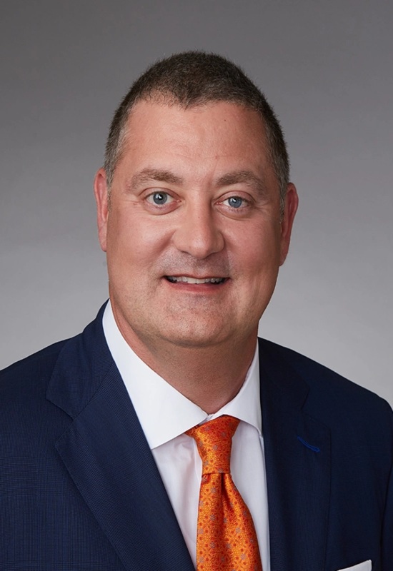 William Beynon, wearing a navy suit with a white shirt and bright orange tie, President and CEO at Capital Wealth Advisors
