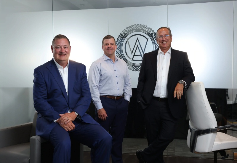 Three individuals in formal business attire standing and sitting at the Capital Wealth Advisors office in Naples, FL.