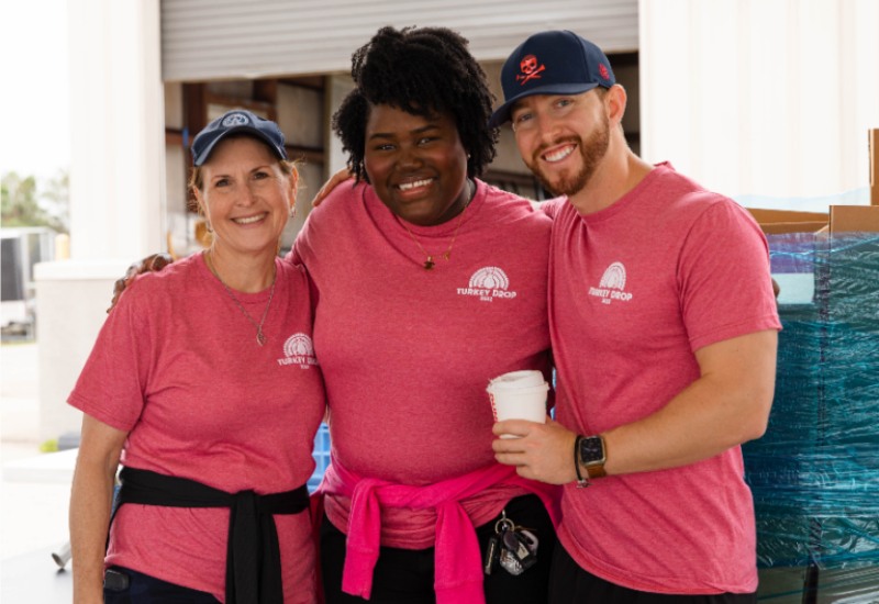 Three team members in matching red shirts standing together during a community event at Capital Wealth Advisors